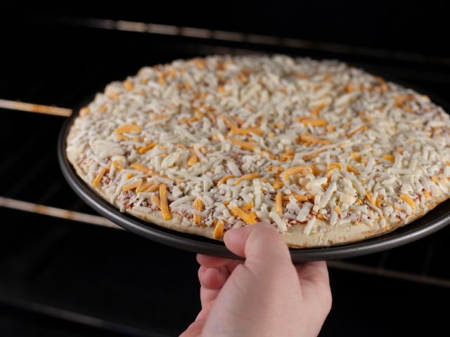 Person putting frozen pizza in oven